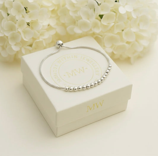 Silver bracelet on a white Memory Within jewelry box, against a soft floral background.