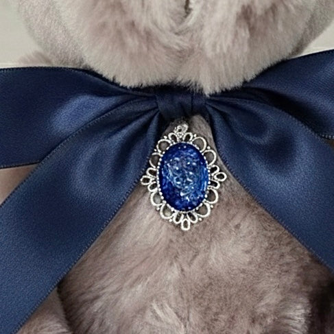 Close-up of a teddy bear with a blue ribbon and decorative brooch on a light background
