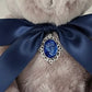 Close-up of a teddy bear with a blue ribbon and decorative brooch on a light background