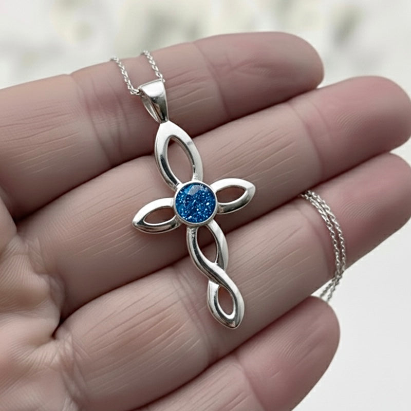 Silver cross ashes keepsake pendant with blue gemstone held in a hand