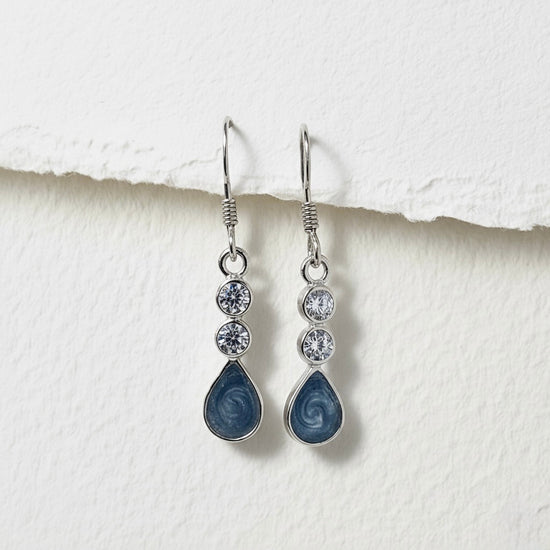 Pair of blue teardrop earrings with silver accents on a textured white surface