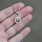 Teardrop-shaped ashes keepsake pendant with purple stone and clear stones on a chain held in a hand.