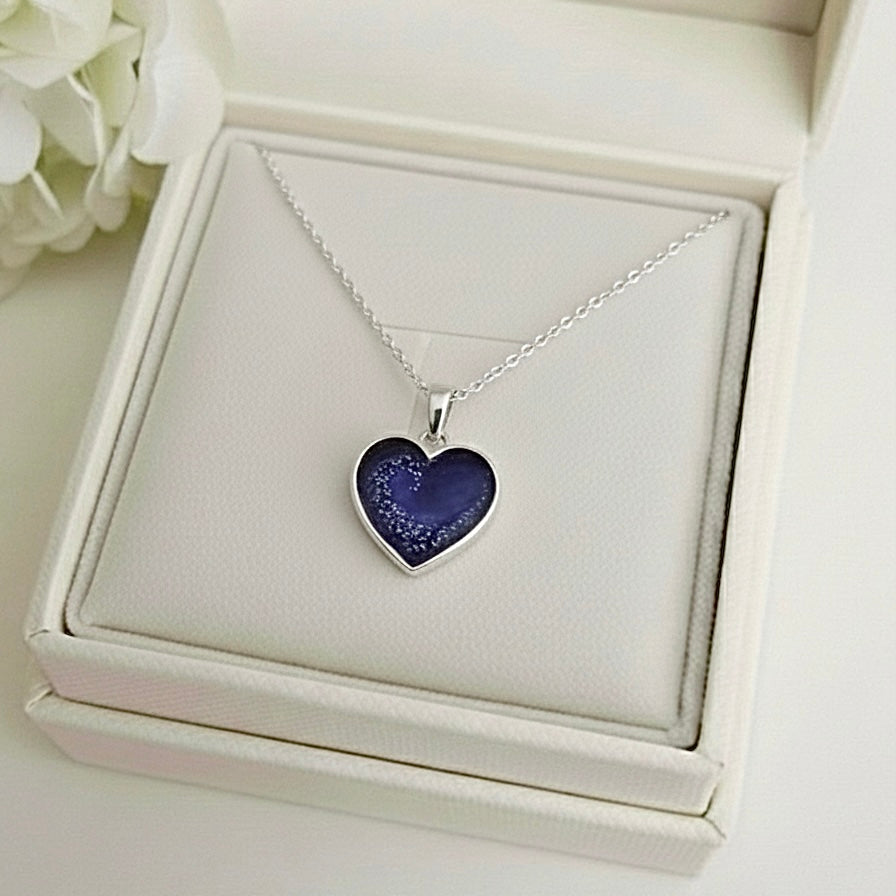 Heart-shaped purple ashes keepsake pendant necklace in a white memory within jewelry box with white flowers in the background