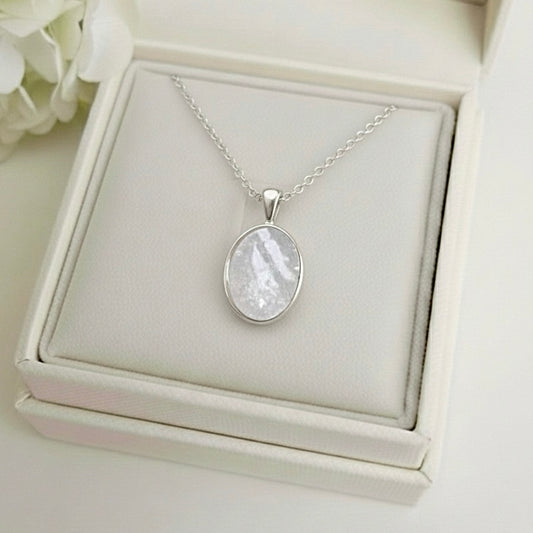 Silver necklace with an ashes keepsake pendant on a white jewelry box