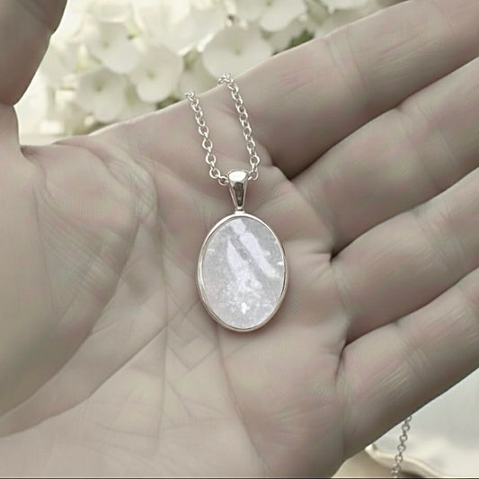 Silver necklace with an ashes keepsake pendant held in a hand against a blurred floral background