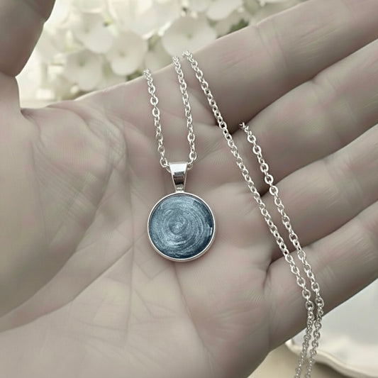 Silver necklace with a round ashes keepsake pendant held in a hand against a blurred floral background