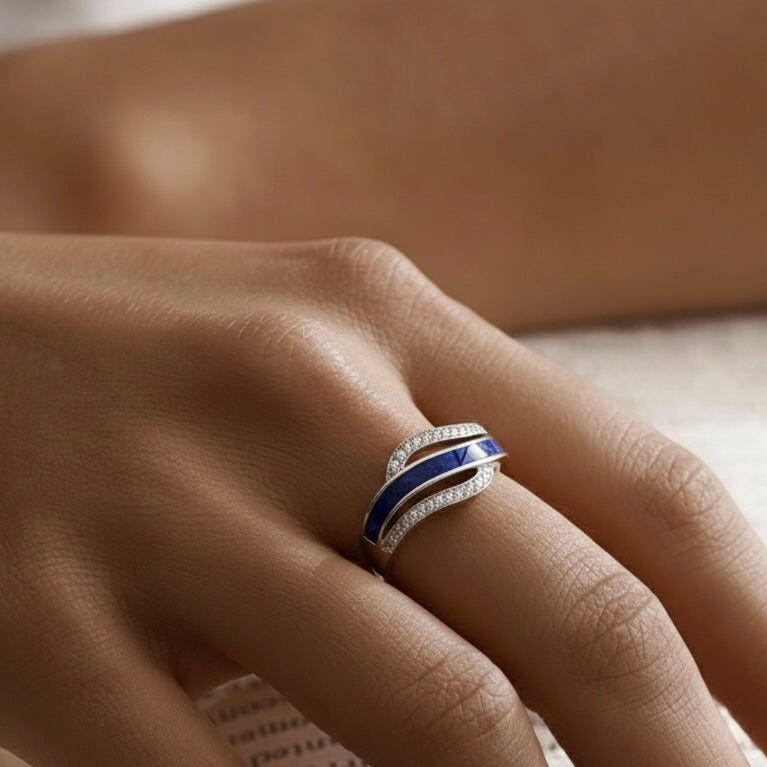 Close-up of a hand wearing a silver and blue ashes keepsake ring on a blurred background