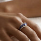 Close-up of a hand wearing a silver and blue ashes keepsake ring on a blurred background
