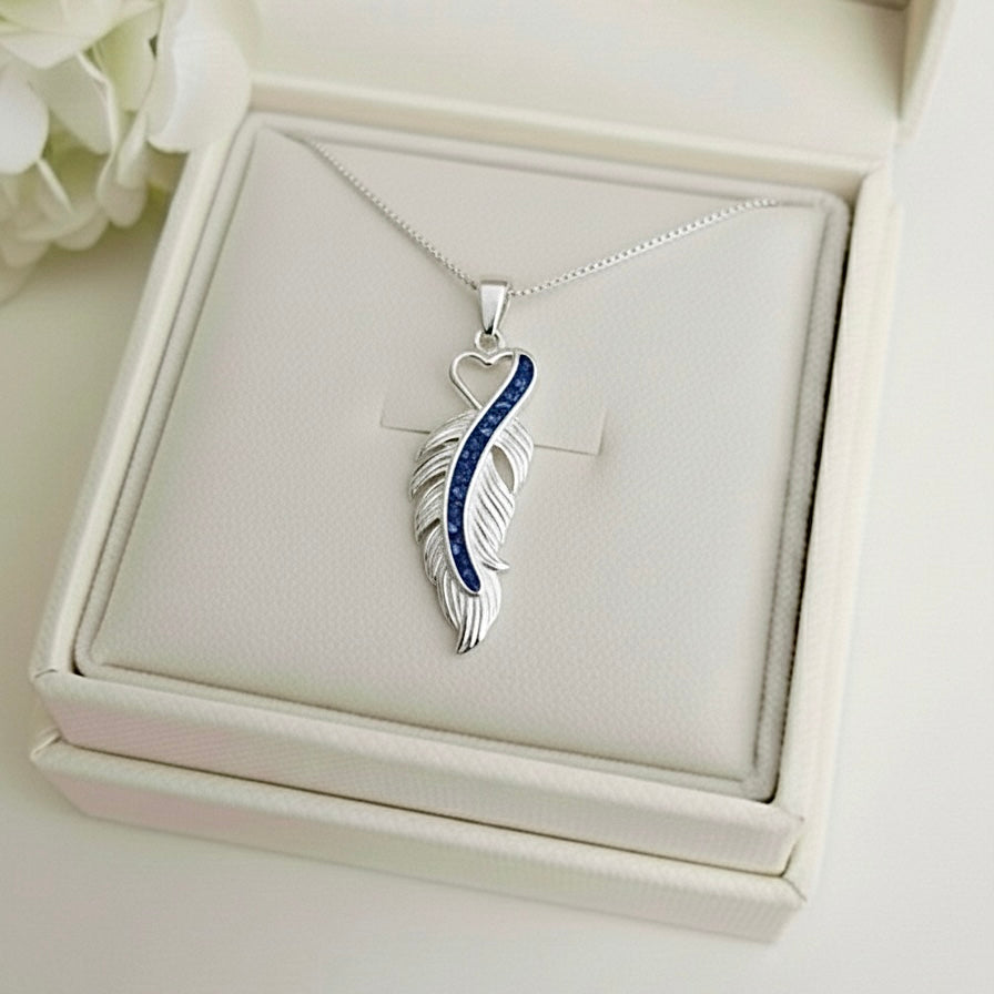 Silver feather-shaped ashes keepsake pendant with blue accents on a white Memory Within jewelry box