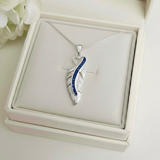 Silver feather-shaped ashes keepsake pendant with blue accents on a white Memory Within jewelry box