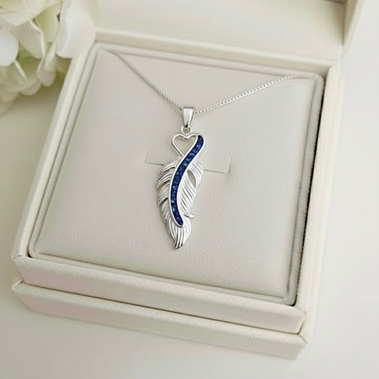 Silver feather-shaped ashes keepsake pendant with blue accents on a white Memory Within jewelry box