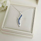 Silver feather-shaped ashes keepsake pendant with blue accents on a white Memory Within jewelry box