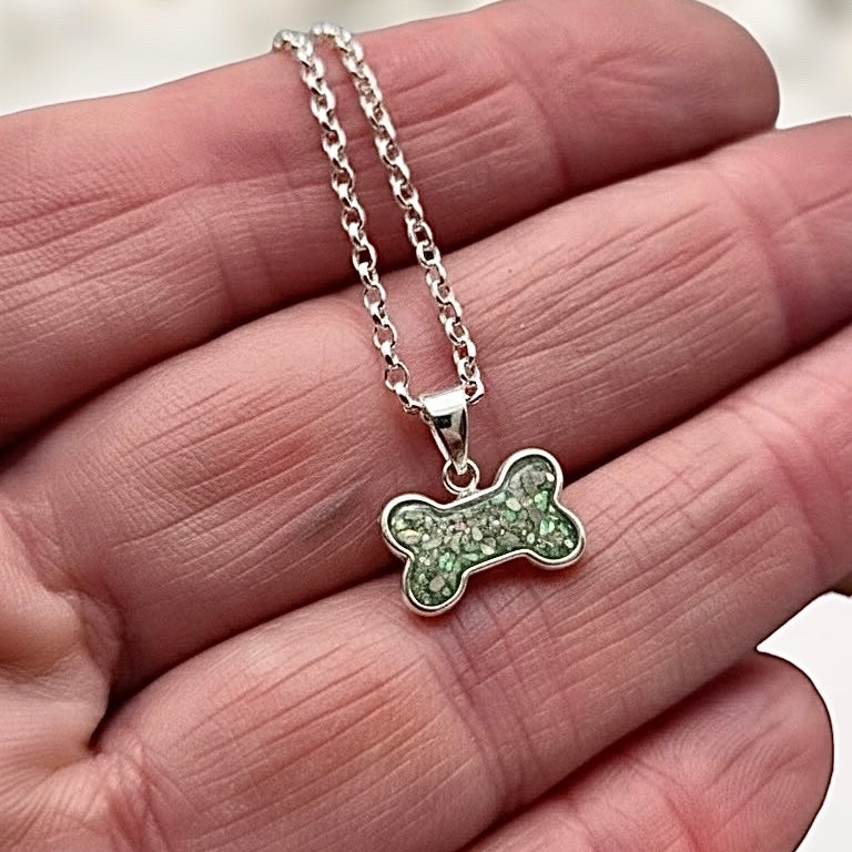 Silver necklace with a green bone shape ashes keepsake pendant held between fingers