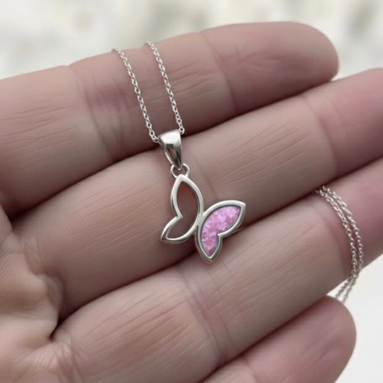 Butterfly-shaped necklace with pink center held between fingers