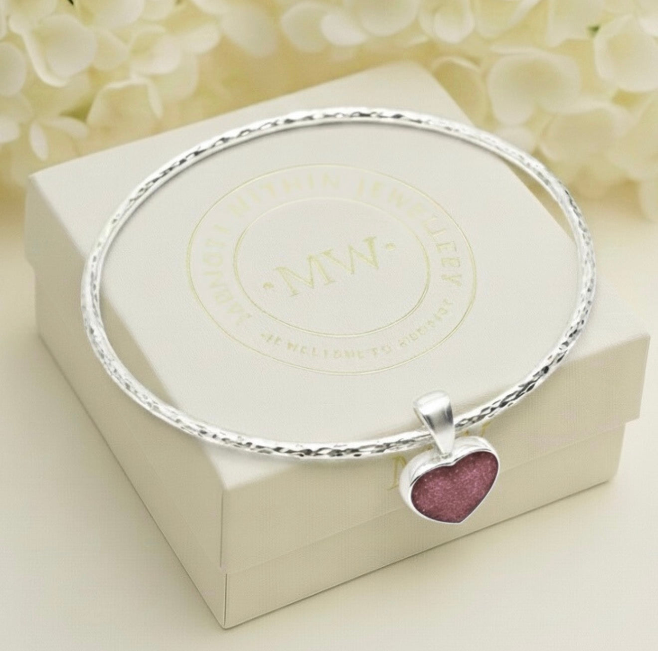Silver bracelet with a heart-shaped ashes keepsake charm on a white box with Memory Within branding.
