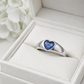 Silver ring with a blue heart ashes keepsake stone in a white memory within jewelry box.