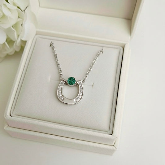 Silver horseshoe necklace with a green ashes gemstone on a white memory within jewelry box