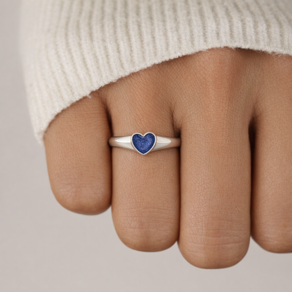 Sterling silver heart signet ring with blue heart, worn on the finger.