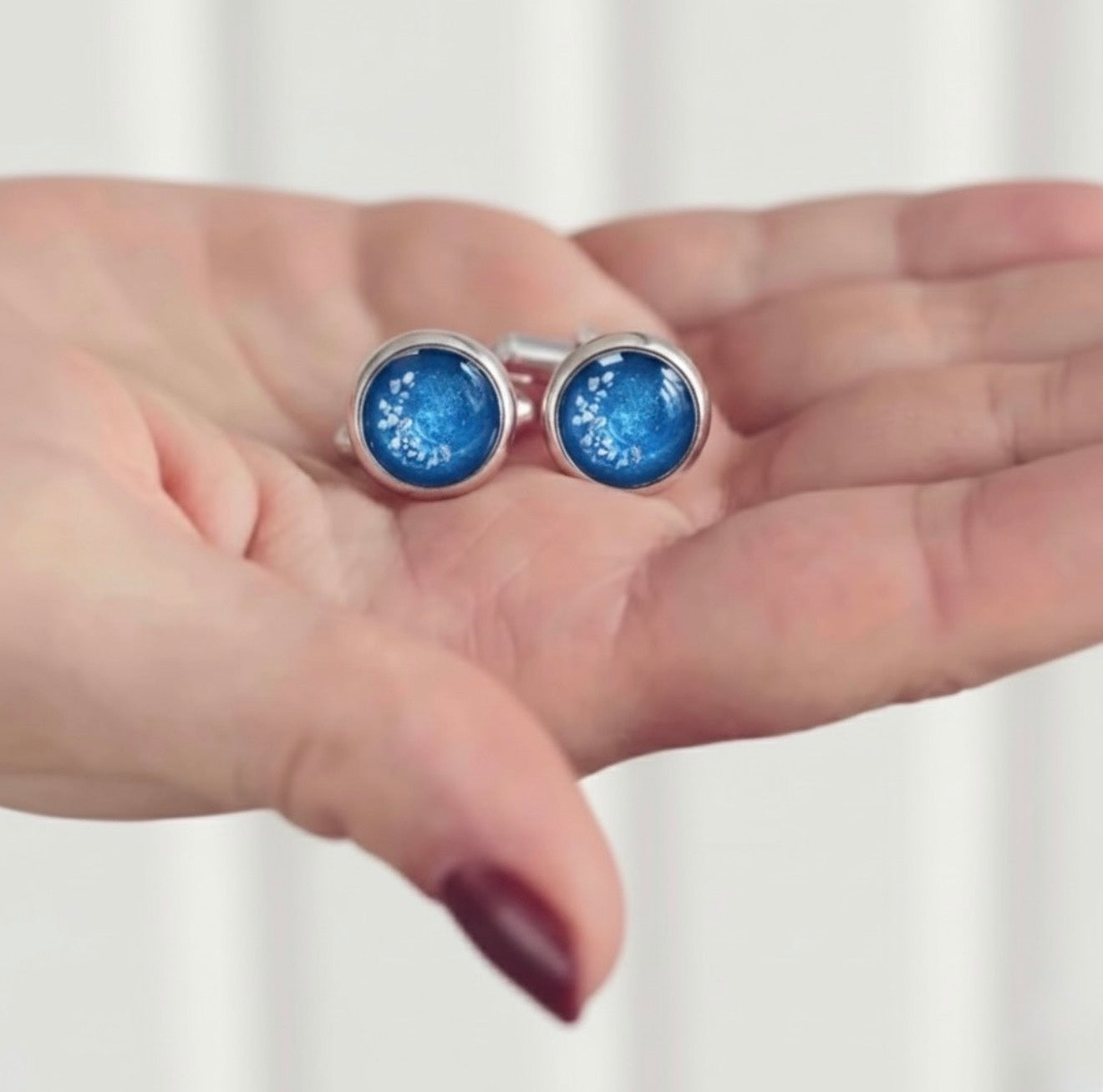 Blue round ashes memorial cufflinks held in a hand against a white background