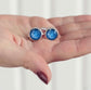 Blue round ashes memorial cufflinks held in a hand against a white background