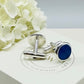Silver cufflinks with blue ashes keepsake stones on a white memory within box with flowers in the background