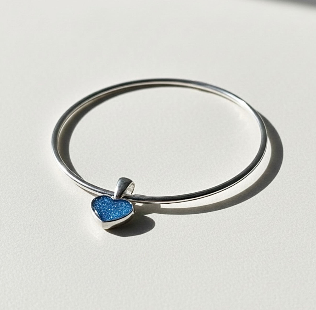Silver bracelet with a blue heart-shaped ashes keepsake charm on a light gray background