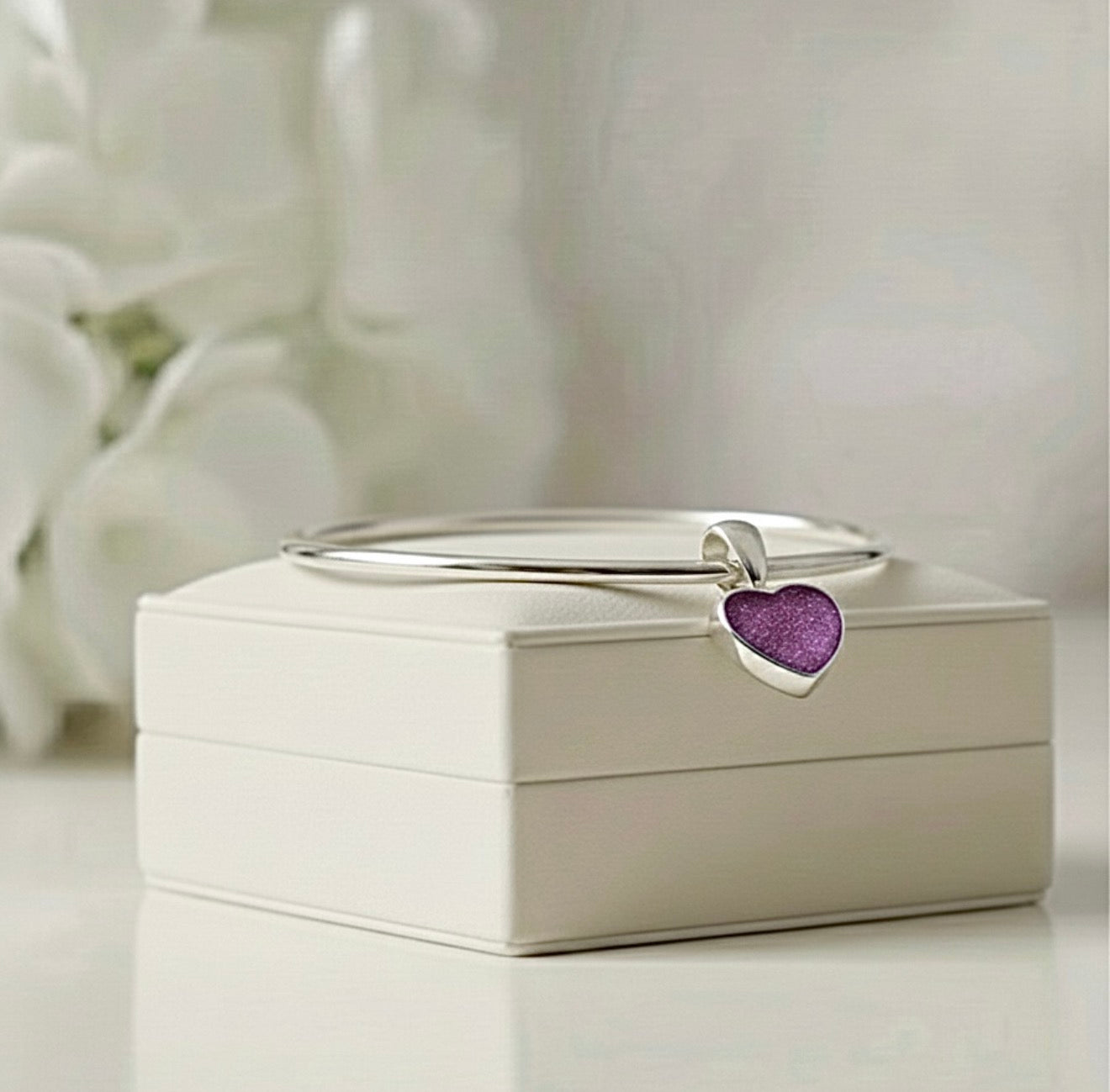 Silver bangle with a purple heart-shaped ashes keepsake charm on a white Memory Within jewelry box.