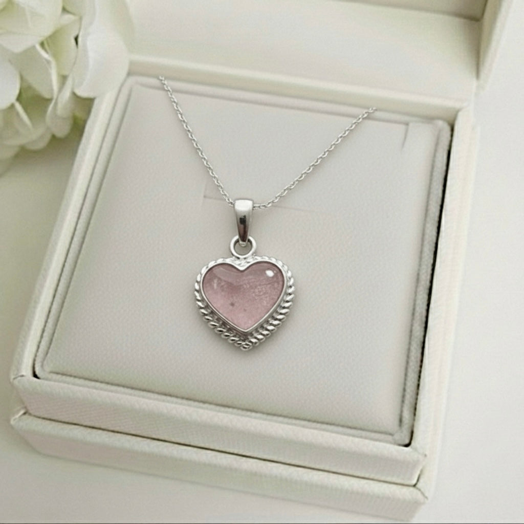 Heart-shaped pink ashes keepsake pendant on a silver chain in a memory within jewelry box with white flowers in the background