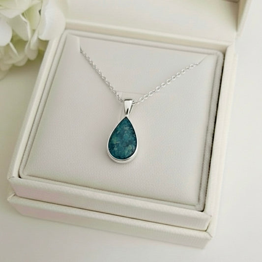 Teardrop-shaped ashes keepsake pendant necklace on a white memory within jewelry box with flowers in the background